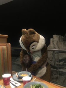 Young white boy hugging the character of Chip, a giant chipmunk, in front of a table with food.