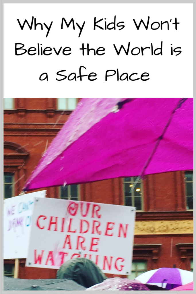 Photo: People with umbrellas and a sign that says "Our children are watching" Text: Why My Kids Won't Believe the World is a Safe Place