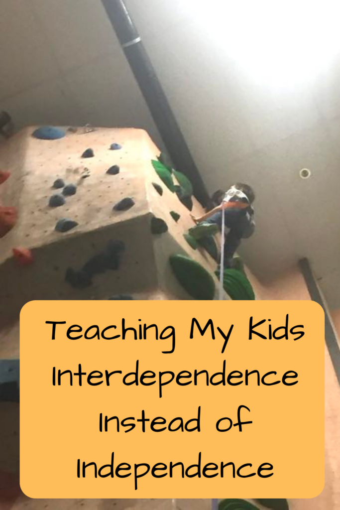 Teaching My Kids Interdependence Instead of Independence; photo of a kid climbing a rock-climbing wall and almost being at the top