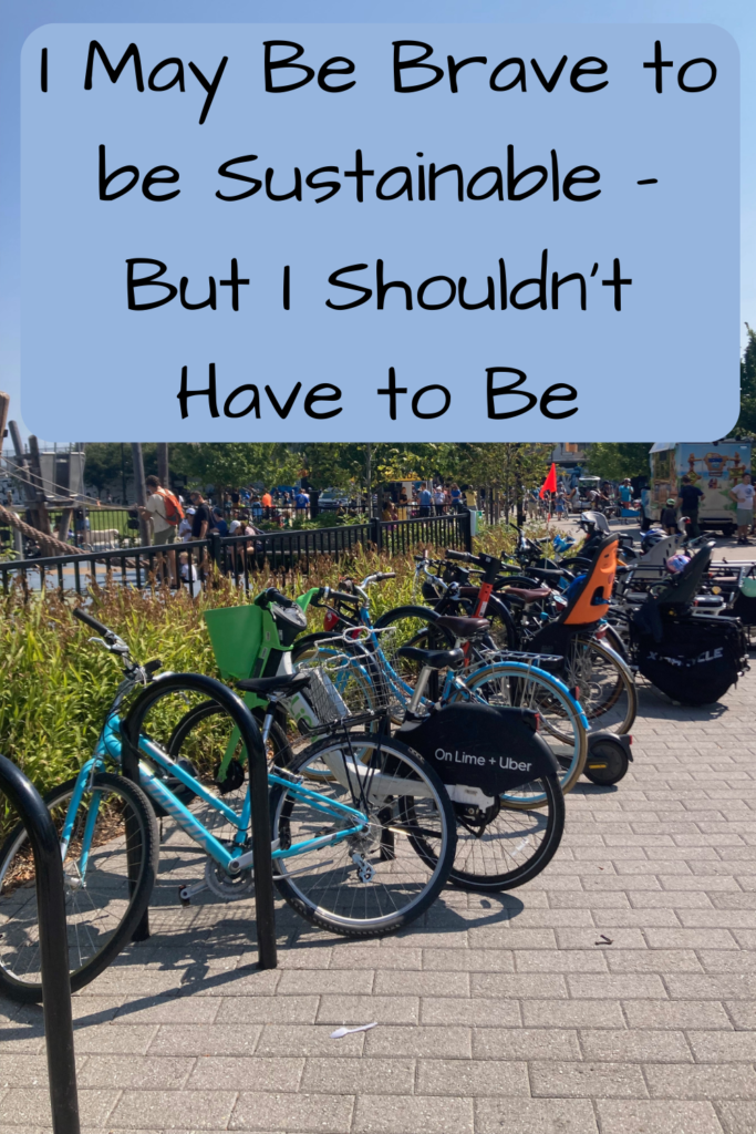 I May Be Brave to be Sustainable - But I Shouldn't Have to Be; Photo of a number of bikes - bike share, bikes with kids' seats, cargo bikes - parked on bike racks outside a park with a playground