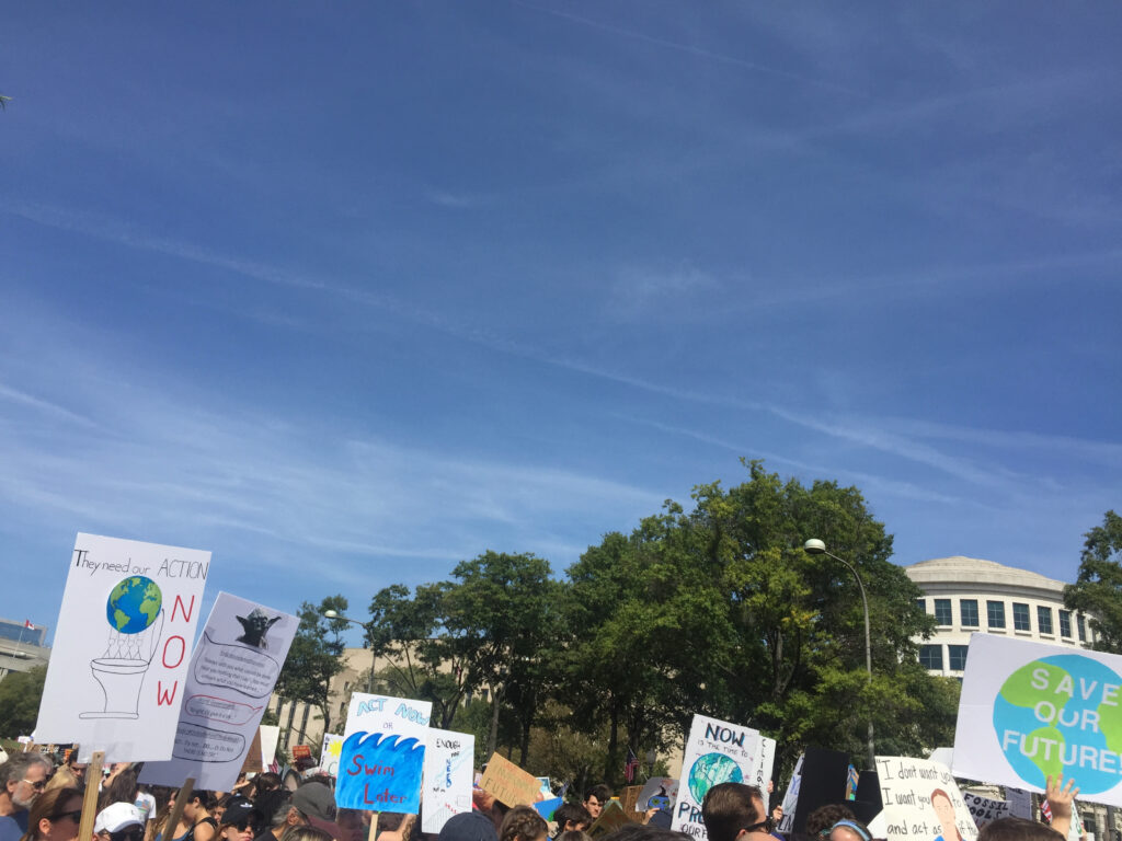 Photo of a group gathered for a climate march with signs saying they need your action now, save our future, etc.