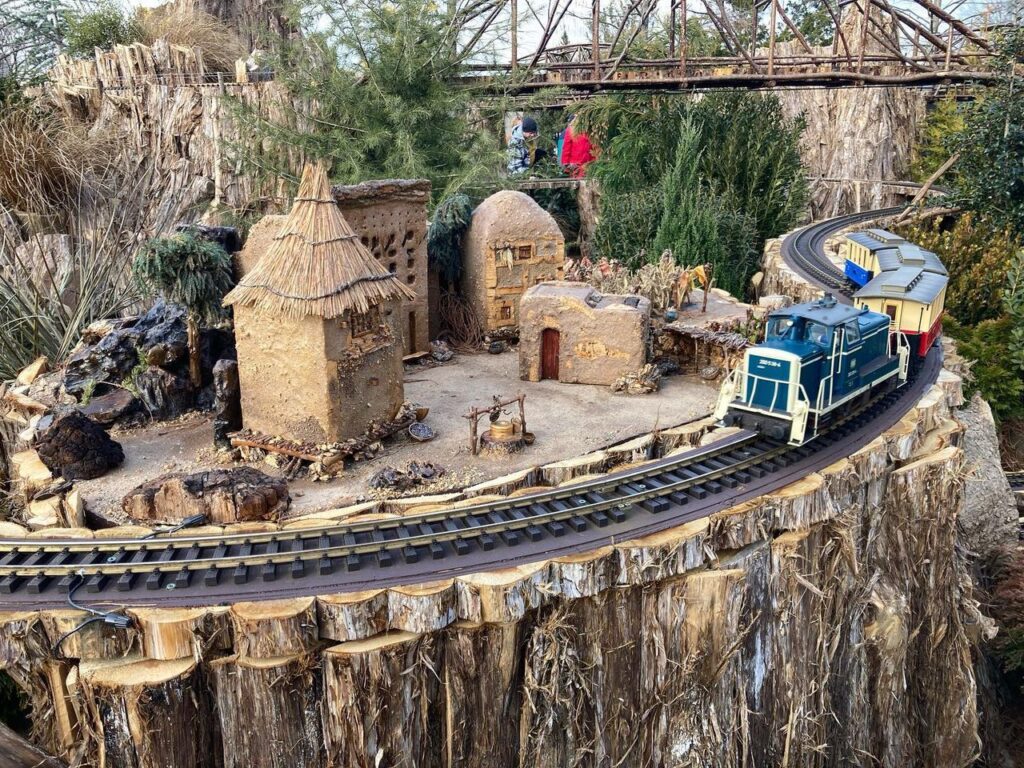 Photo of a model train going past a model of a farm in Mali made of plant parts