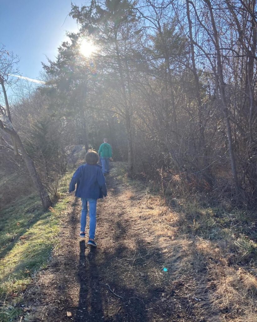 Photo of a kid in a blue fleece jacket (my son) and older man in a green sweatshirt (my dad) walking down a hiking path with trees on both sides