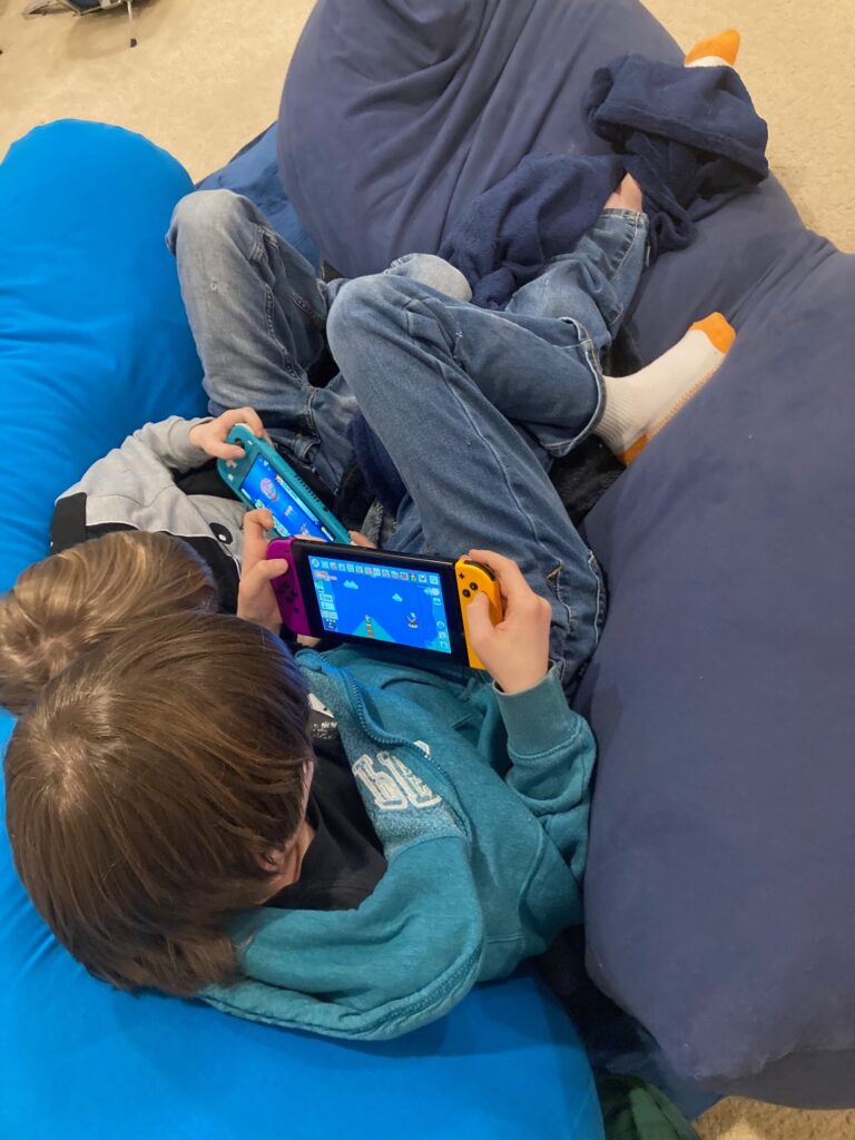 Photo of two white boys cuddled together on a giant bean bag, both playing separate Nintendo Switches
