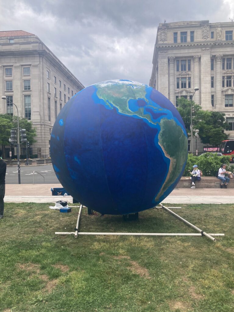A giant inflatable globe sitting on grass in Washington D.C. with formal buildings behind it