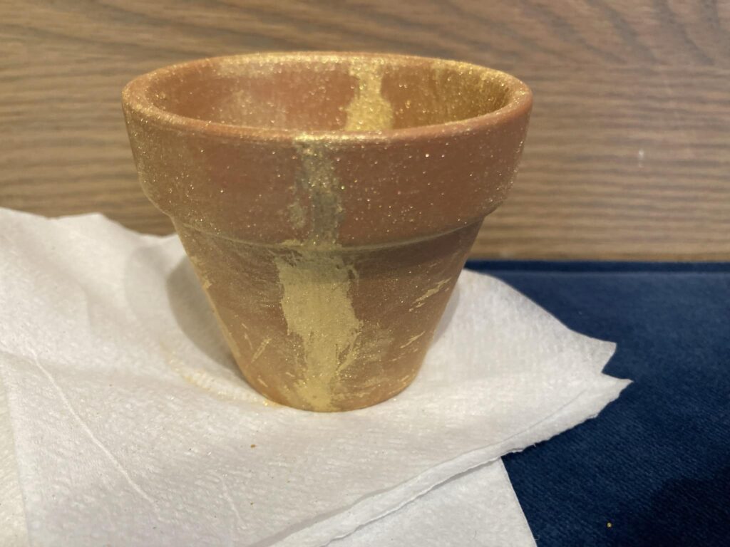 A brown flower pot that has globs of gold paint on it