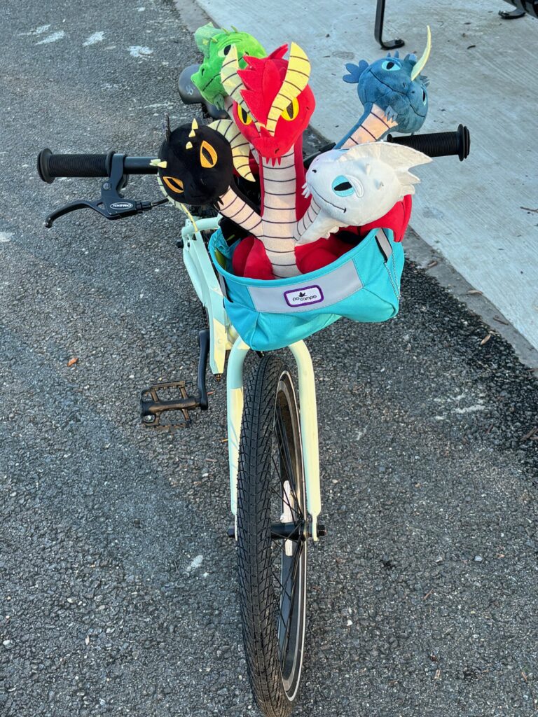 A children's bicycle with a blue bag on the handlebars and a five-headed stuffed dragon in the bag