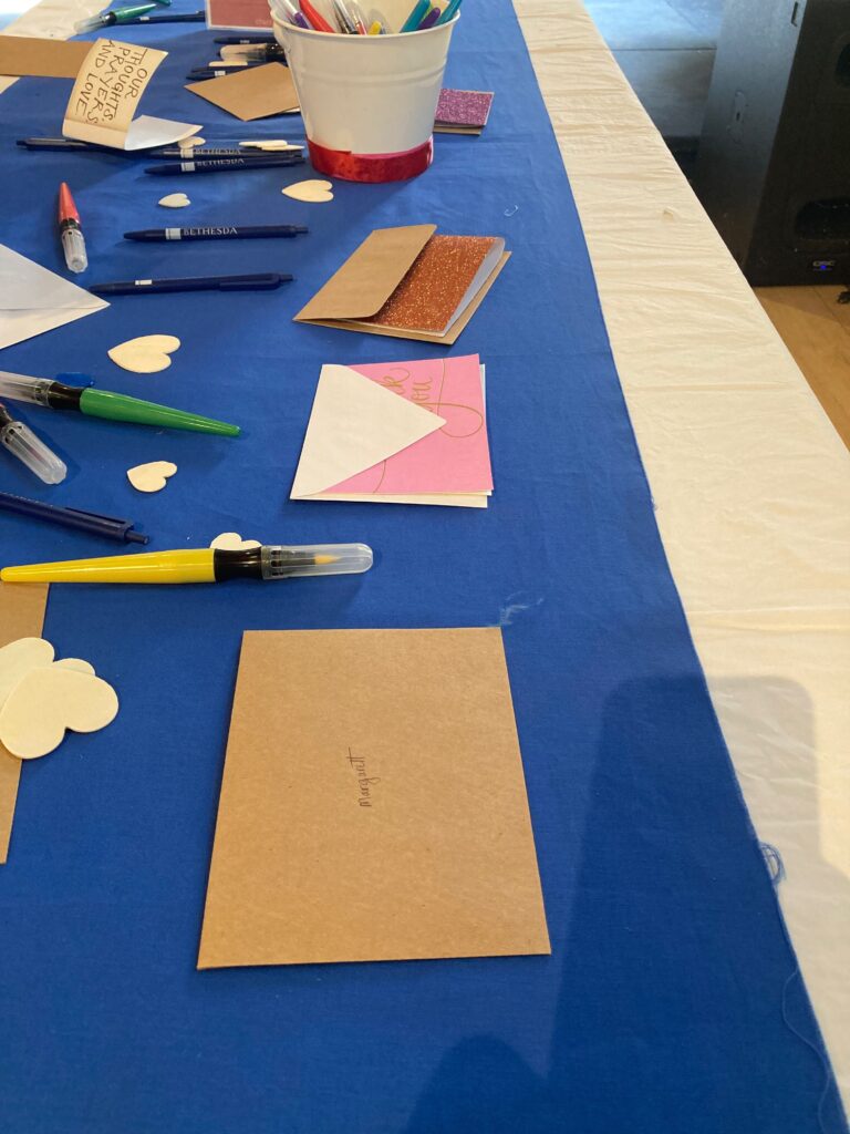 A table with a blue tablecloth on it and cards and multi-colored pens all over it